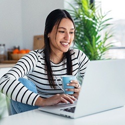 Woman smiling while drinking coffee and looking at laptop