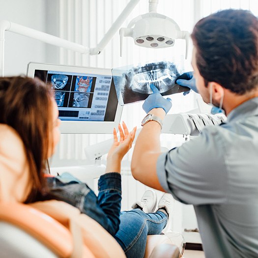 a dentist showing a patient her X-rays while she sits in a dental chair