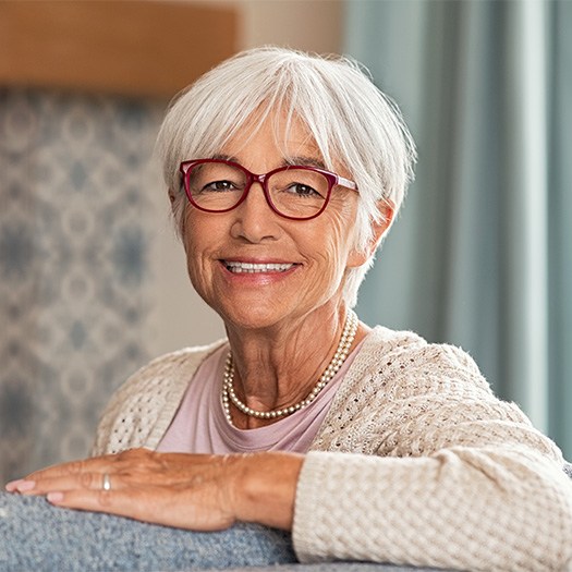 Senior woman in glasses sitting on couch smiling