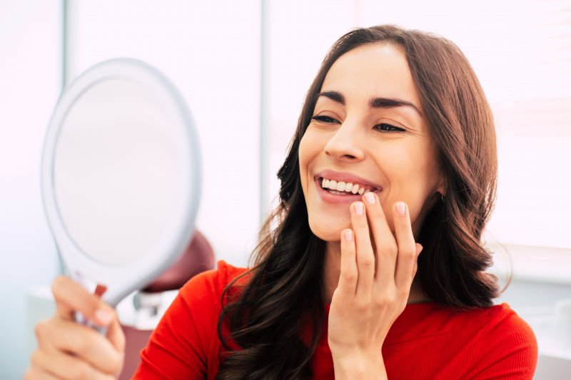 A woman admiring her new dental implants in a hand mirror